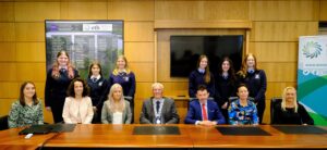 Large group of people sitting and standing behind a desk. 