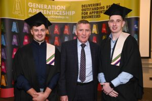 Two graduates standing side by side with a man standing in between the.