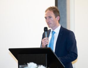 Man speaking at a lectern, holding a microphone.