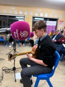 Student playing guitar and Highland Radio microphone. 