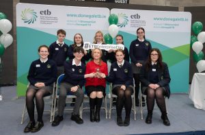 Group of students and an adult sitting and standing, with a trophy. 