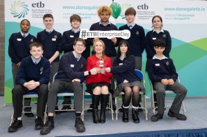 Group of students and an adult sitting and standing, with a trophy. 