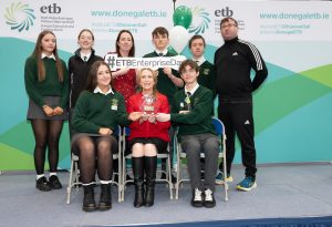 Group of students and an adult sitting and standing, with a trophy. 