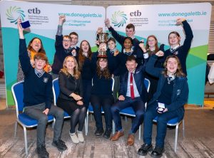 Group of students and adults holding a cup and arms in the air.