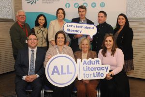 Group of people sitting and standing in front of a banner and some are holding signs. 