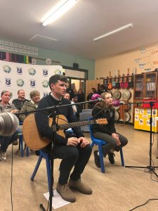 Two people sitting behind microphones, one holding a guitar. 