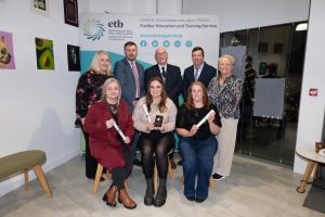 Group of people sitting and standing, some holding awards.