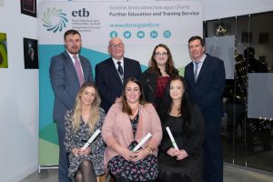 Group of people sitting and standing, some holding awards.